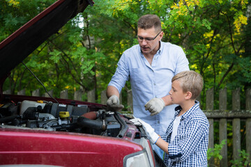 Dad and his son repairing car with open hood outdoors, fixing engine - 386535257