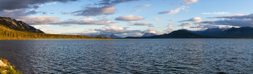Panoramic View of Scenic Lake surrounded by Mountains and Trees on a Cloudy Fall Day at Sunset in Canadian Nature. Taken near Atlin, Yukon, Canada.