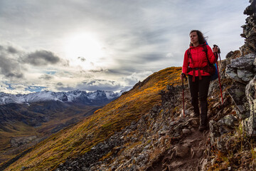 Woman Backpacking along Scenic Hiking Trail surrounded by Mountains in Canadian Nature. Season change from Fall to Winter. Taken in Tombstone Territorial Park, Yukon, Canada.