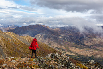 Fototapeta premium Woman Backpacking along Scenic Hiking Trail surrounded by Mountains in Canadian Nature. Taken in Tombstone Territorial Park, Yukon, Canada.