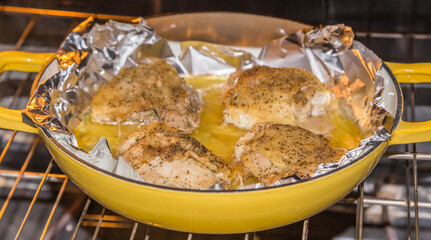 Seasoned baked chicken thighs in an aluminum foil lined yellow Dutch oven on a rack in its natural...