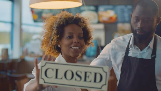 African cheerful small business owners smiling and turning open sign on cafe glass door