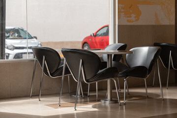 interior of a restaurant, with black and metal table chairs, next to a window with sun