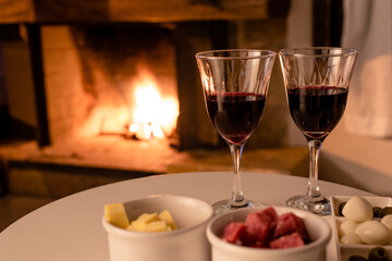 two glasses of wine, cheese, salami, olives and quail eggs in front of a fireplace