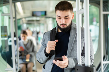 Portrait of focused young man using mobile phone while traveling by modern city bus in autumn day