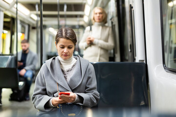 Positive woman reading from mobile phone screen in tram. High quality photo