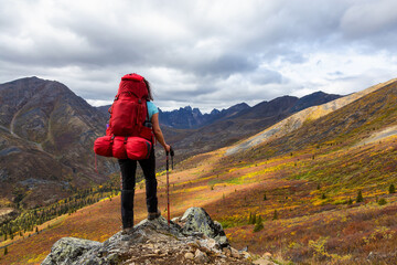 Obraz premium Woman Standing on Rocks looking at Scenic Mountain Peaks and Valley during Fall in Canadian Nature. Taken in Tombstone Territorial Park, Yukon, Canada.