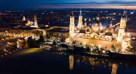 Fototapeta na wymiar Aerial view of lighted Roman Catholic Basilica Our Lady of Pillar on background of Zaragoza cityscape and Ebro river at dusk, Spain..
