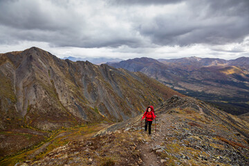 Fototapeta premium Woman Backpacking on Scenic Rocky Hiking Trail surrounded by Mountains during Fall in Canadian Nature. Taken in Tombstone Territorial Park, Yukon, Canada.