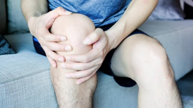 Knee pain .man sitting on the bed  Her hand caught at the knee. Having painful feet and stretching muscles fatigue To relieve pain. health concepts.