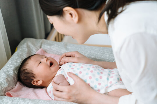 portrait of asian baby feeling comfortable after changing diaper and laughing to her mother happily. chinese woman is interacting with her kid on baby changing.