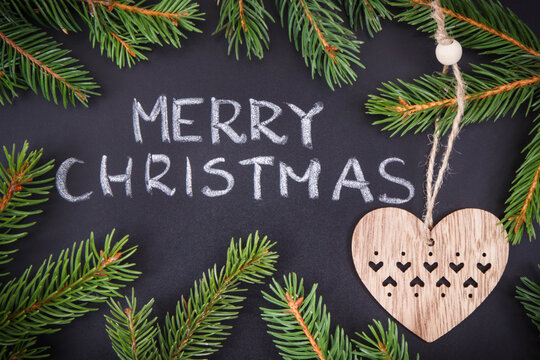 Inscription Merry Christmas, spruce branches and heart shape on black background. Decoration for christmas time