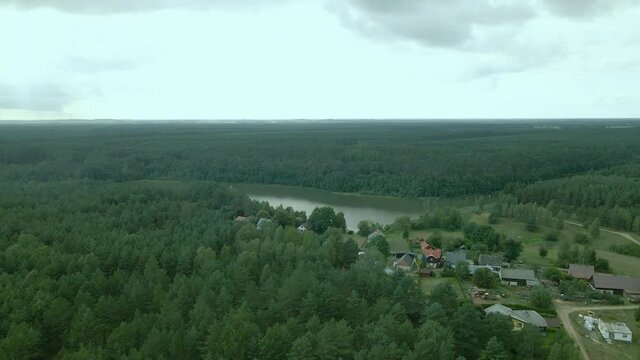 Aerial fly over private houses and cottages located on the bank of Okierskie lake, dense green leafy deciduous forest in Kowalskie Blota village, Poland, forward motion, drone shot