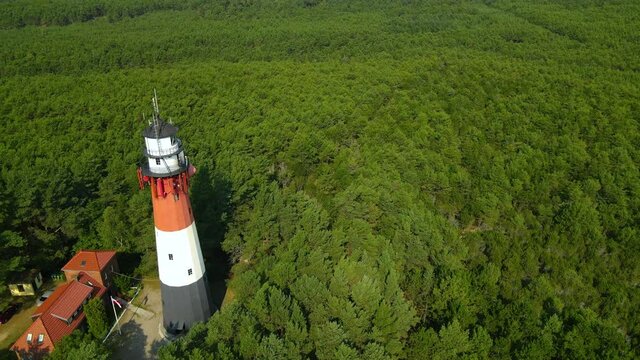 The drone slow pulls out and reveals Stilo Lighthouse and green forest around it - lighthouse located in Osetnik on the Polish coast of the Baltic Sea, close to the village of Sasino, aerial close-up
