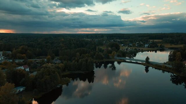 Flying over Kowalskie Blota village at sunset, Dramatic clouds, clouds reflections on the tranquil water surface; private houses and cottages located on the bank of Okierskie lake, Poland