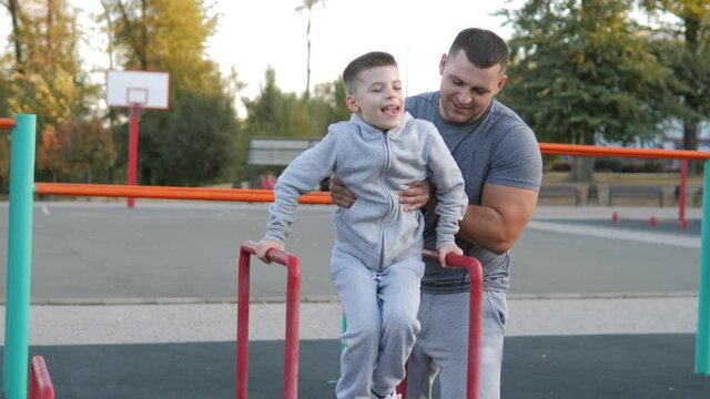 Healthy family, parental support and sports for kids concept. Father with son doing exercises on steel bar on sport ground