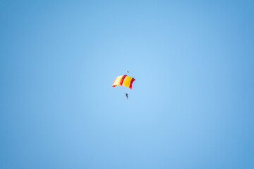One parachutist floats slowly at low altitude on the background of clear sky
