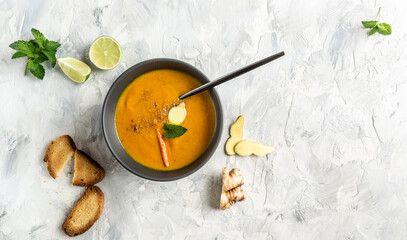 Carrot soup with ginger and coriander soup with baked peppers and cheese, lime juice and ginger on a light background