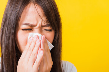 Portrait of Asian beautiful young woman sad she crying wipe the mucus with tissue, Close up of pretty girl sneezing sinus using towel to wipe snot from nose, studio shot isolated on yellow background