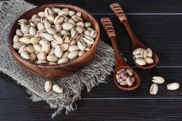 fried pistachios in a wooden bowl and spoon on the table kind of above. delicious snack in the form of fried pistachios. background with pistachios close-up.