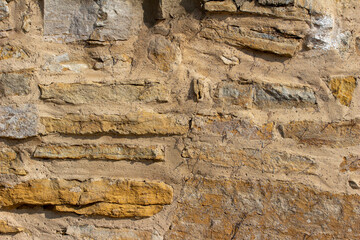 Full frame abstract texture background of a shabby chic antique tan color rugged stone wall with natural stones and thick cement mortar