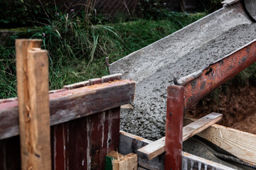 The concrete mixer unloads the concrete through a chute into a timber formwork with metal...