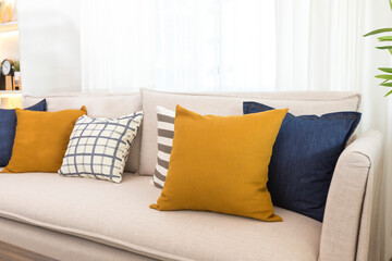 Blue and yellow pillows on a white sofa with glass vase and plant pot on table, living room interior.