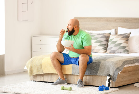 Overweight man eating chips at home. Weight loss concept