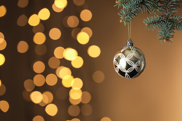 Ball hanging on Christmas tree branch against color background with blurred lights