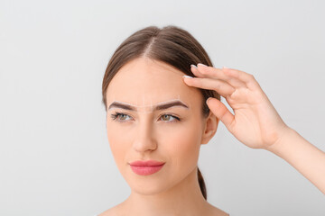 Young woman with marking for eyebrow correction against light background