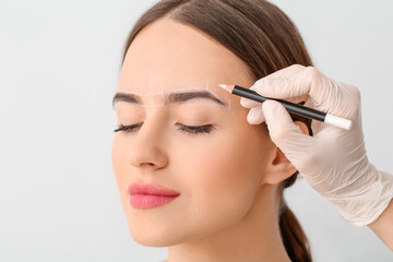 Young woman undergoing eyebrow correction procedure on light background