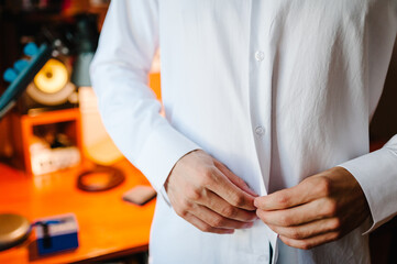 Man wearing white shirt in room at home. Men's hands buttons on a white shirt.