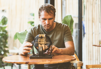 Young man in green shirt hold lotto sphere spins small balls, table loto game as symbol of future problem life crisis choice. Look into, sad thoughtful face invented idea. Real skin. Matt photo toned