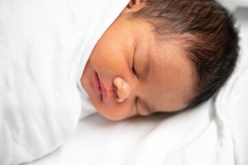 A newborn baby sleeps in a white swaddle