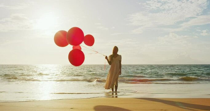 Beautiful happy young woman holding red balloons on the beach