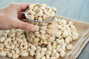 Hand with pistachio nuts in transparent glass jar on a wooden table. Healthy food high protein.