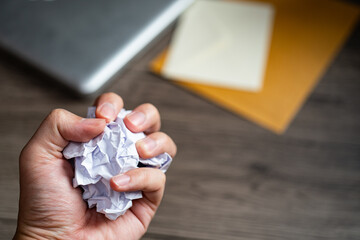 Crumpled balls of white paper in hand over wooden table, workspace.