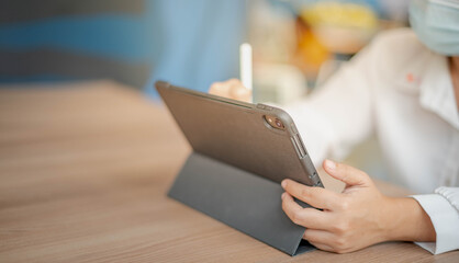 The woman wearing mask and drawing with the pencil on the Ipad.