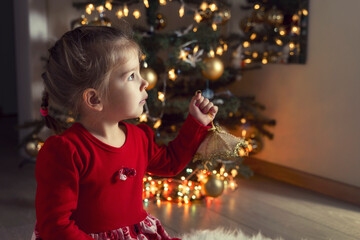 cute little girl in red dress at home by the christmas tree