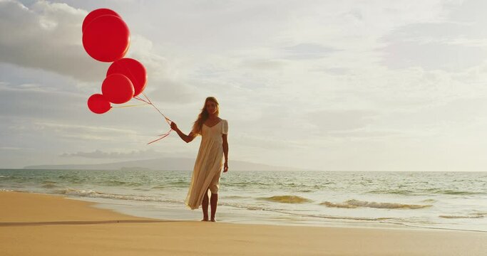 Beautiful happy young woman holding red balloons on the beach, happiness and wellness concept