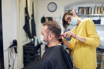 Hairdresser and customer in a salon with medical masks during virus pandemic. Working with safety mask.