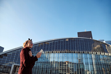 Woman using cellphone in urban surroundings with skyscrapers.