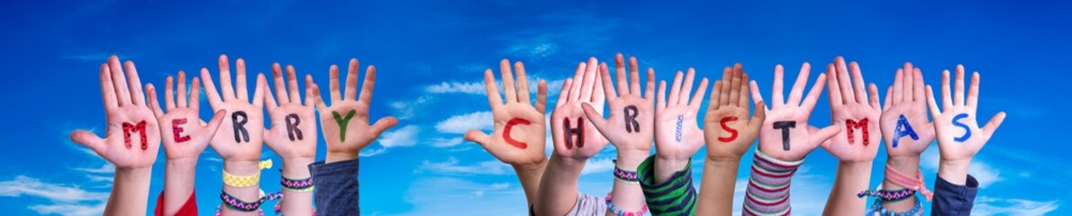 Children Hands Building Colorful English Word Merry Christmas. Blue Sky As Background