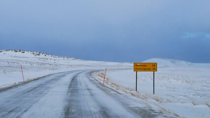 Fototapeta premium Icy road E69 (European route) with road sign displaying the distance to Nordkapp of 68 km near Repvag, Troms og Finnmark, Norway with red snowplow markings and snow-covered landscape in winter time.