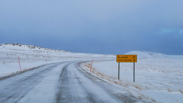 Icy road E69 (European route) with road sign displaying the distance to Nordkapp of 68 km near Repvag, Troms og Finnmark, Norway with red snowplow markings and snow-covered landscape in winter time.