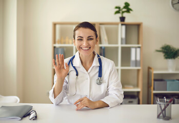 Young smiling doctor therapist looking at camera and greeting somebody online