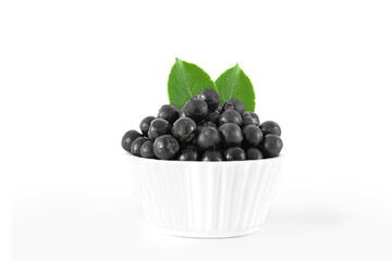 Black chokeberry with green leaves in a ceramic bowl,isolated on a white background.