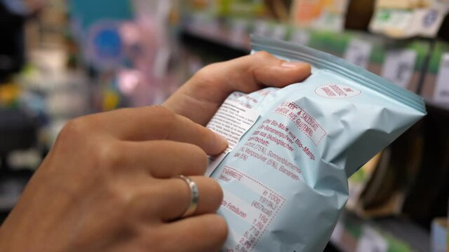 Close up of two hands holding packaged product in store to read ingredients contents. Shopping concept