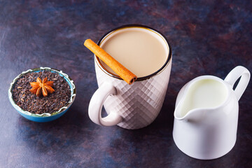 Masala chai tea. Traditional indian drink - masala tea with spices on dark background. Ceramic cup of spices tea and white milk jug