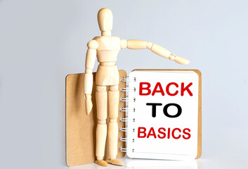 Wooden man shows with a hand to white notepad with text BACK TO BASICS